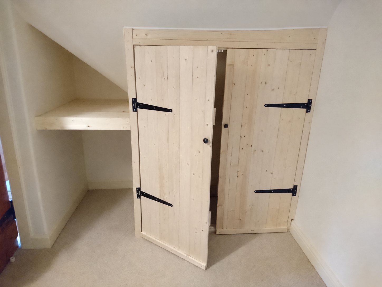 Fitted timber cupboard and shelving beneath a sloping ceiling