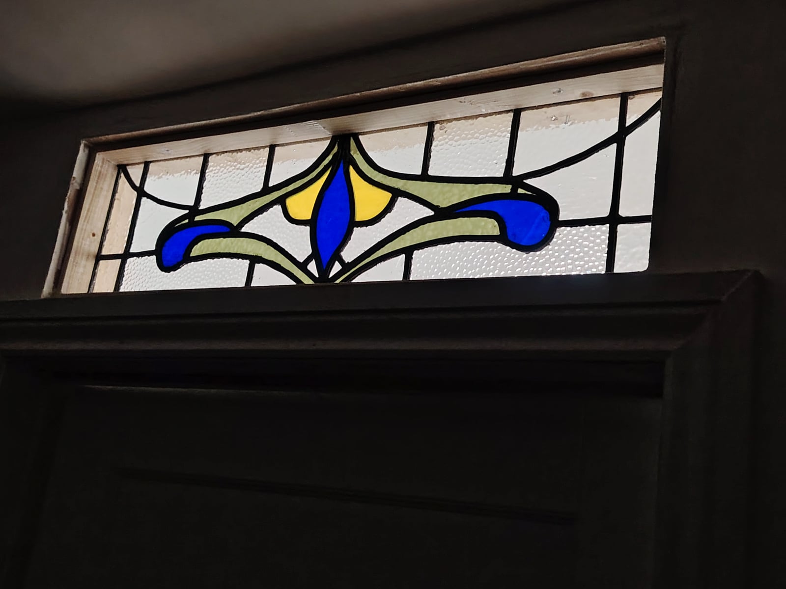 Blue, yellow and green stained-glass panel above a doorway.